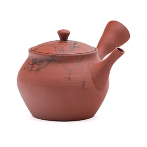 May include: A terracotta teapot with a brown lid and a spout. The teapot has a crackled glaze and a unique design.