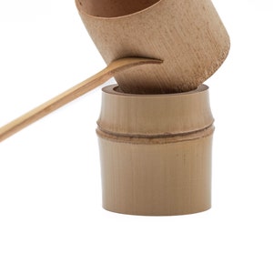 May include: A set of two brown bamboo scoops for serving tea or other beverages. The larger scoop is resting on top of the smaller scoop.