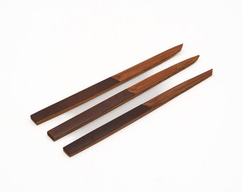 Op de afbeelding: Drie houten spiesjes met donkerbruin hout aan het ene uiteinde en lichtbruin hout aan het andere uiteinde.