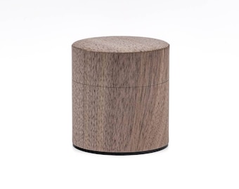 Puede incluir: Una caja de madera cilíndrica con un acabado de madera de grano marrón oscuro. La caja tiene una tapa y está hecha de madera maciza.