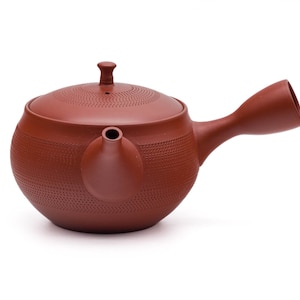 Könnte beinhalten: Eine rote Ton-Teekanne mit einer strukturierten Oberfläche und einem kurzen Ausguss. Die Teekanne hat einen Deckel und einen Griff, der zur Seite ragt.