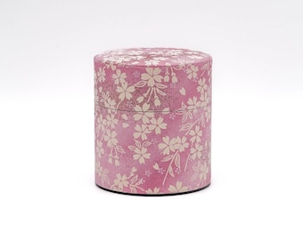 May include: A pink cylindrical container with a white floral pattern. The container is made of paper and has a smooth surface.