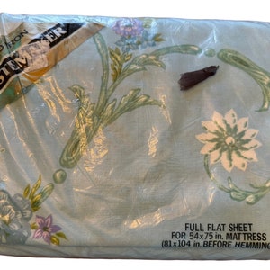 Puede incluir: Una sábana plana de color azul claro con un patrón floral en tonos verdes, blancos y rosas. La sábana está empaquetada en plástico y etiquetada con "No Iron Tastemaker" y "Full Flat Sheet for 54x75 in. Mattress (81x104 in. Before Hemming)".