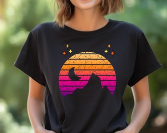 Puede incluir: Una camiseta negra con un gráfico de puesta de sol retro que presenta una cordillera, una luna creciente y estrellas. El gráfico está en tonos de naranja, rosa y amarillo.