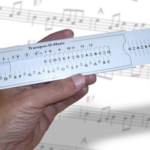 May include: A white plastic Transpos-O-Matic musical key transposition tool with a sliding scale and a ruler. The tool is labeled with musical notes and numbers from 1 to 13.