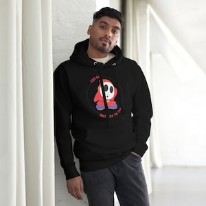 May include: Black hooded sweatshirt with a graphic of a Shy Guy character from the Super Mario video game series. The graphic features the text "Shy Guy" and "Not Shy to Try".