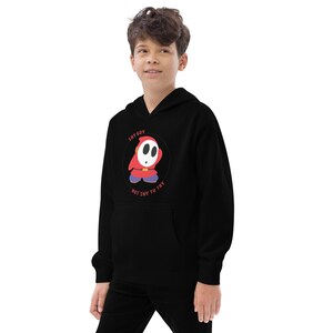 May include: Black hooded sweatshirt with a graphic of Shy Guy from the Super Mario franchise. The graphic is a circle with the text "Shy Guy" and "Not Shy To Try" around the image of Shy Guy.