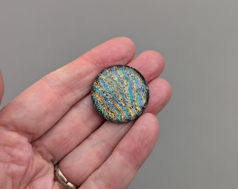 May include: A round, iridescent glass tile with a black background and gold and blue swirls.