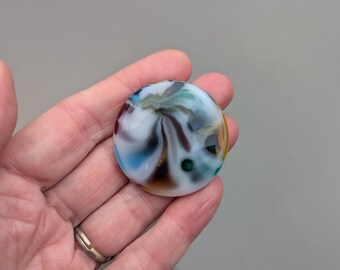 May include: A round, white glass paperweight with swirls of blue, green, brown, and yellow.
