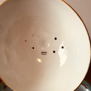 May include: The underside of a white ceramic bowl with a gold rim. The bowl has a small hole in the center and several smaller holes around the edge. The bowl is marked "Limoges France".