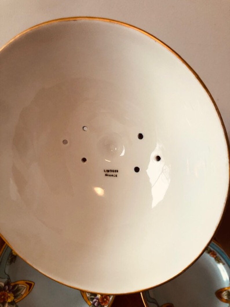 May include: The underside of a white ceramic bowl with a gold rim. The bowl has a small hole in the center and several smaller holes around the edge. The bowl is marked "Limoges France".