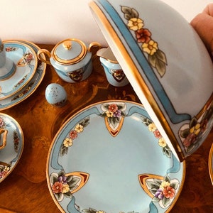 May include: A blue and gold tea set with floral designs. The set includes a teapot, sugar bowl, creamer, and a plate. The tea set is on a wooden table.