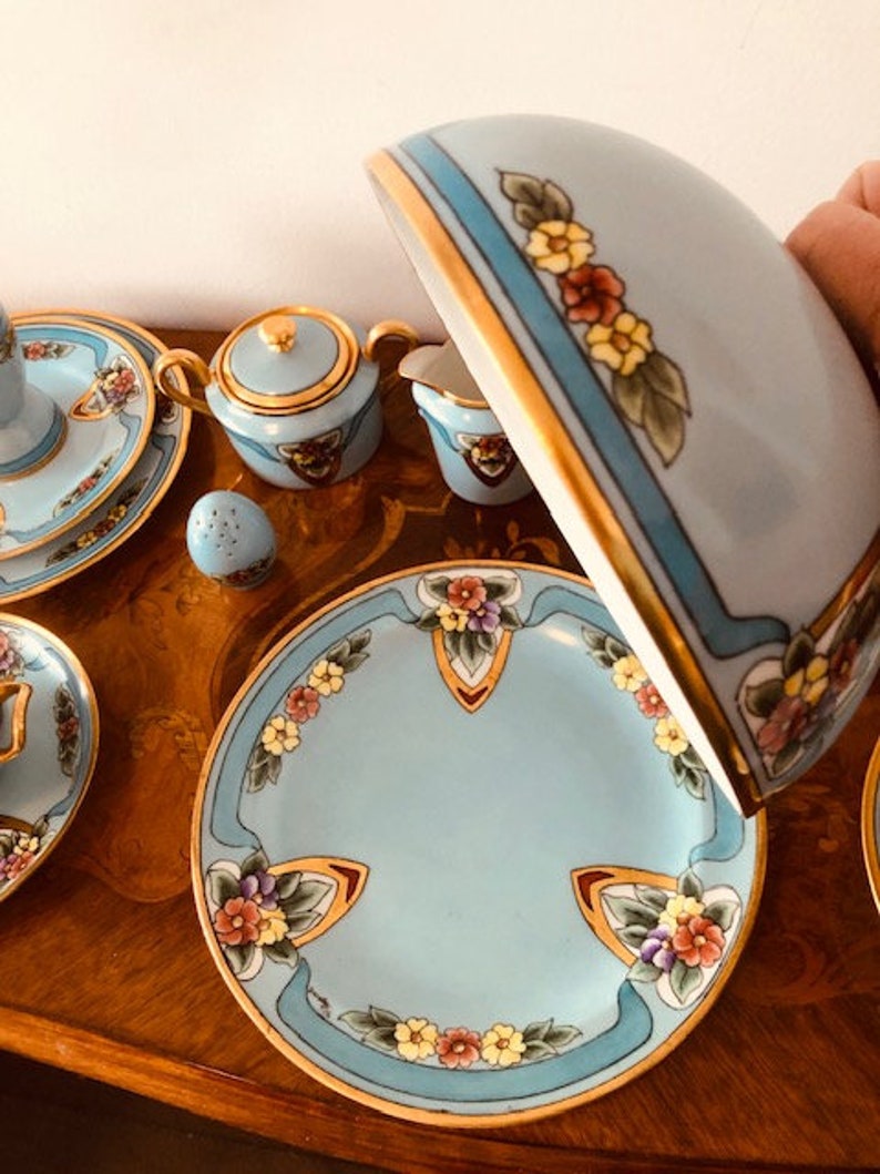 May include: A blue and gold tea set with floral designs. The set includes a teapot, sugar bowl, creamer, and a plate. The tea set is on a wooden table.