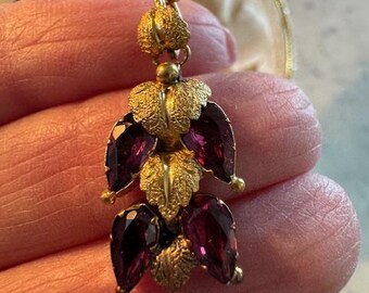 May include: A gold necklace with a pendant featuring a cluster of purple gemstones surrounded by gold leaf-shaped accents.