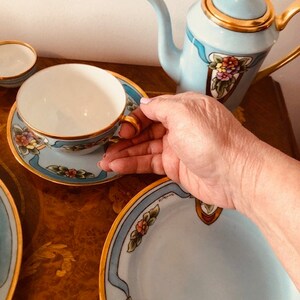 May include: A blue and gold tea set with floral designs. The set includes a teapot, a teacup, a saucer, and a larger plate.