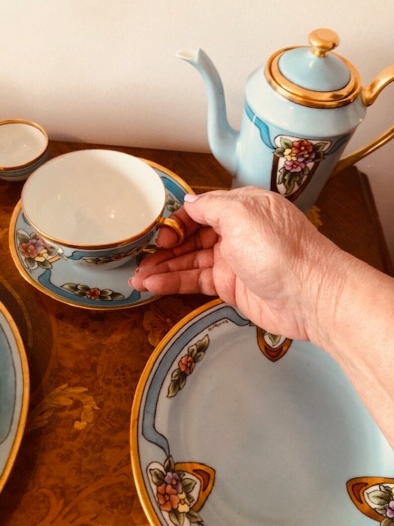 May include: A blue and gold tea set with floral designs. The set includes a teapot, a teacup, a saucer, and a larger plate.