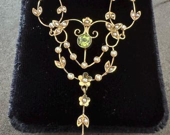 May include: A gold necklace featuring a central round green gemstone and a dangling oval green gemstone. The piece is decorated with small white pearls arranged in floral and leaf-like patterns, connected by delicate gold wire scrollwork.