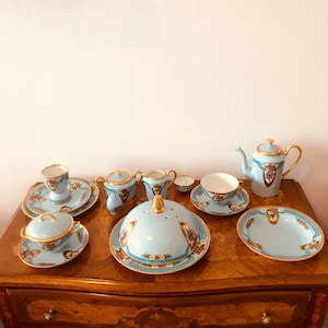May include: A set of blue and white porcelain teacups, saucers, and a teapot with gold accents and floral designs. The set is arranged on a wooden table with drawers.