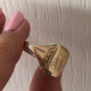 May include: A gold signet ring with an engraved monogram. The ring is worn on a finger.