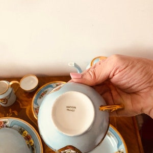 May include: A blue and gold teacup and saucer set with floral designs. The bottom of the teacup has the words "Haviland France" printed on it.