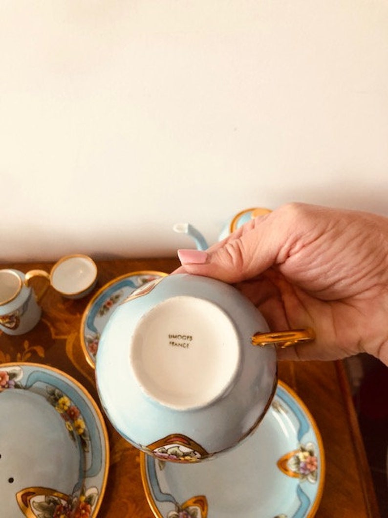 May include: A blue and gold teacup and saucer set with floral designs. The bottom of the teacup has the words "Haviland France" printed on it.