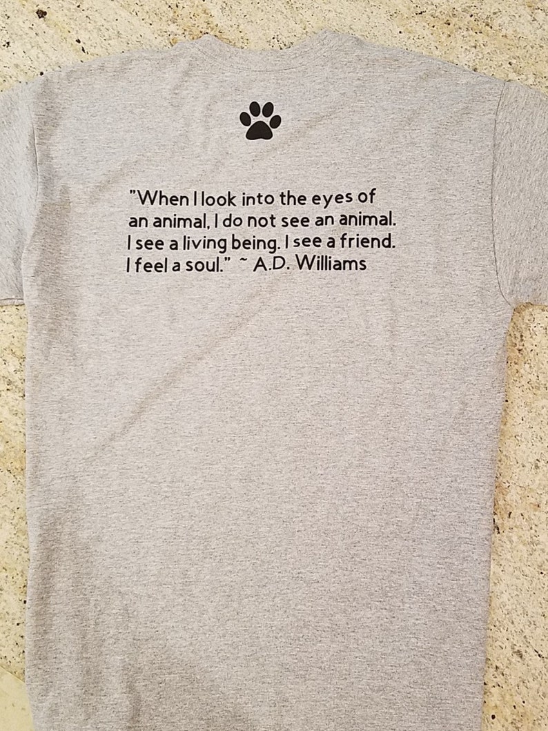 Puede incluir: Camiseta gris con una huella de pata y una cita sobre los animales: "Cuando miro a los ojos de un animal, no veo un animal. Veo un ser vivo. Veo un amigo. Siento un alma." ~ A.D. Williams