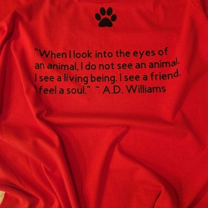 Puede incluir: Camiseta roja con una huella de pata negra y una cita sobre los animales: "Cuando miro a los ojos de un animal, no veo un animal. Veo un ser vivo. Veo un amigo. Siento un alma." ~ A.D. Williams