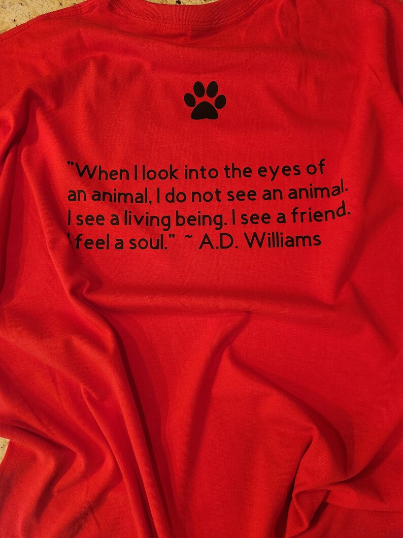 Puede incluir: Camiseta roja con una huella de pata negra y una cita sobre los animales: "Cuando miro a los ojos de un animal, no veo un animal. Veo un ser vivo. Veo un amigo. Siento un alma." ~ A.D. Williams