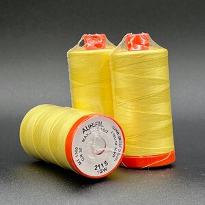 May include: Three spools of yellow thread with red and white labels. The labels read "Aurifil Mako 50/2 100% cotone Mako Made in Italy GR 30 MT 1300 2115 1GW".
