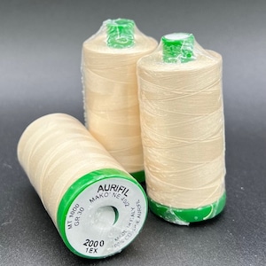 May include: Three spools of white thread with green labels. The label reads "Aurifil Mako' NE 40/2", "MT 1000 GR 30 2000 1EX", and "Made in Italy 100% Cotton Aurifil".
