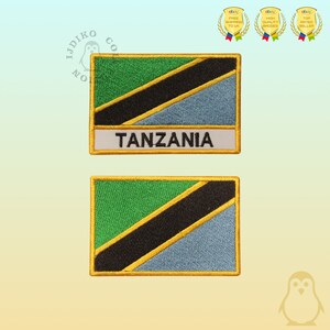 May include: Two rectangular embroidered patches featuring the flag of Tanzania. The flag design includes green, black, blue, and yellow colors. The word "TANZANIA" is embroidered in white on a white background.