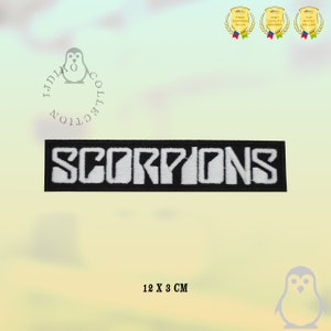 May include: Black and white embroidered patch with the word "SCORPIONS" in white lettering on a black background. The patch is 12 cm by 3 cm.