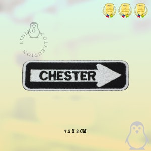 Op de afbeelding: Zwart-witte geborduurde patch met een witte pijl die naar rechts wijst en het woord "CHESTER" in witte tekst. De patch is 7,5 cm bij 3 cm.