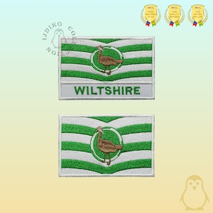 Könnte beinhalten: Zwei gestickte Aufnäher mit der Flagge von Wiltshire, England. Die Aufnäher sind weiß mit grünen und weißen Streifen und einem braunen Vogel in einem Kreis. Der Text "WILTSHIRE" ist in weiß auf weißem Hintergrund unter der Flagge geschrieben.