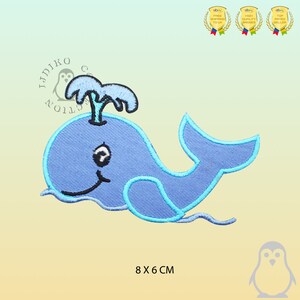 May include: Blue whale applique with a water spout on top. The whale has a smiling face and is outlined in light blue. The applique is 8 cm by 6 cm.