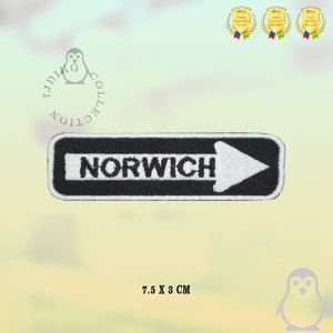 May include: Black and white embroidered iron-on patch with the word "NORWICH" and a white arrow pointing to the right. The patch is 7.5 cm by 3 cm.
