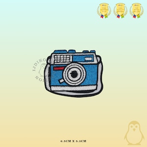 Peut inclure: Patch brodée thermocollante bleu et blanc représentant un appareil photo avec une bande rouge et une sangle. Le patch mesure 6,5 cm sur 5,3 cm.