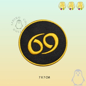 May include: A black and gold embroidered patch featuring the number 69 in a stylised font. The patch is circular and measures 7 cm in diameter.