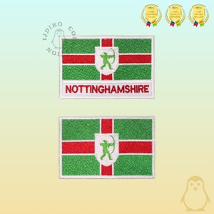 Könnte beinhalten: Zwei gestickte Aufnäher mit der Flagge von Nottinghamshire, England. Die Flagge ist grün mit einem roten Kreuz und einem weißen Schild mit einem grünen Bogenschützen in der Mitte. Der Text "NOTTINGHAMSHIRE" ist in weiß unter der Flagge auf dem oberen Aufnäher geschrieben.