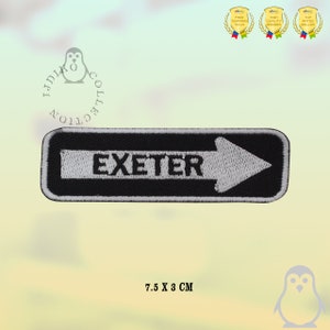 May include: Black and white embroidered patch with the word "EXETER" and a white arrow pointing to the right. The patch is 7.5 inches by 3 inches.