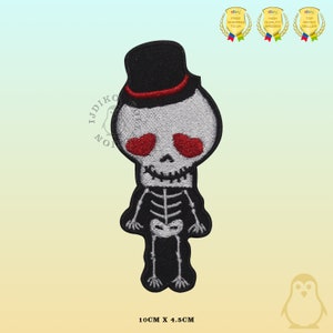 Puede incluir: Un parche bordado para planchar de un esqueleto de dibujos animados que lleva un sombrero de copa negro con una banda roja. El esqueleto tiene ojos rojos y una sonrisa de dientes. El parche mide 10 cm por 4,5 cm.