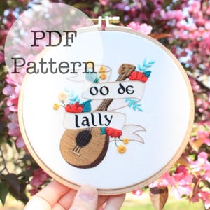 Puede incluir: Arte de aro bordado con un diseño de ukelele. El diseño incluye los textos "oo de lally" y "lally" en pancartas, con acentos florales rojos y amarillos. Las palabras "PDF Pattern" están en la parte superior.