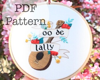 以下が含まれることがあります： ウクレレのデザインが施された刺繍フープアート。デザインには、「oo de lally」と「lally」の文字がバナーに書かれており、赤と黄色の花のアクセントが付いています。「PDF Pattern」の文字が上部にあります。
