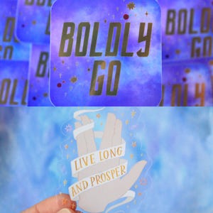 Puede incluir: Una pegatina cuadrada con fondo de galaxia morado y azul con el texto dorado BOLDLY GO. Debajo, una pegatina troquelada muestra una mano en un gesto de saludo con los dedos separados y una cinta blanca con el texto dorado LIVE LONG AND PROSPER.