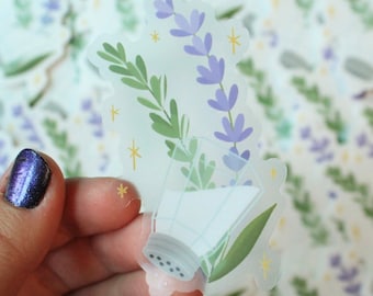 May include: A clear sticker with a lavender sprig and a salt shaker. The sticker has a translucent background and a white outline. The lavender sprig is purple and green, and the salt shaker is white with a black top.
