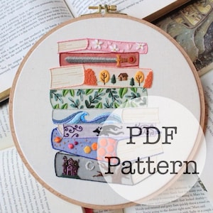May include: An embroidered hoop art piece featuring a stack of colorful books. Each book cover is decorated with unique designs, including flowers, trees, and a castle. The text "PDF Pattern" is overlaid on the image.