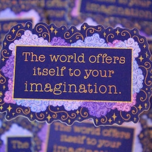 May include: A sticker with the text "The world offers itself to your imagination." The text is in gold on a dark blue background, framed by a decorative border with clouds and stars. The sticker has a scalloped edge.