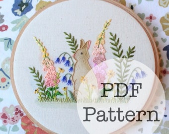 May include: Embroidered hoop art featuring a brown bunny rabbit surrounded by pink, purple, and yellow flowers. The hoop is on a floral fabric background. The text "PDF Pattern" is superimposed on the image.