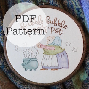 Könnte beinhalten: Ein PDF-Stickmuster in einem Holzrahmen, das eine Hexe und einen brodelnden Topf zeigt. Das Design enthält den Text "Bubble Pot" und "PDF Pattern". Die Hexe trägt einen blauen Hut, ein grünes Oberteil und einen lila Rock.