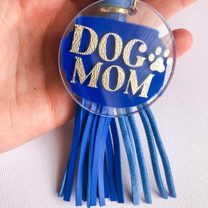 May include: Blue and gold keychain with a clear circle charm that says "DOG MOM" with a paw print. The charm is attached to a blue tassel.